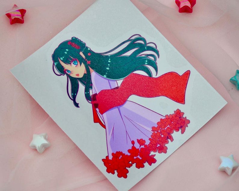 May include: A sticker featuring a cartoon illustration of a woman with long, dark green hair wearing a purple dress and a red scarf. She is surrounded by red flowers.
