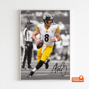 May include: Framed black and white photograph of a football player in a yellow and white uniform, number 8, running with the ball. The player is wearing a helmet and the image includes a signature.