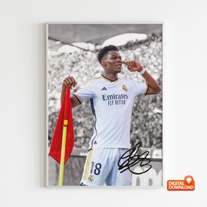 Könnte beinhalten: Ein Fußballspieler in einem weißen Trikot mit dem Text "Emirates Fly Better" und der Nummer 18 auf dem Rücken. Er hält eine rote Flagge und schaut nach rechts. Der Hintergrund ist ein verschwommenes Bild einer Menschenmenge.
