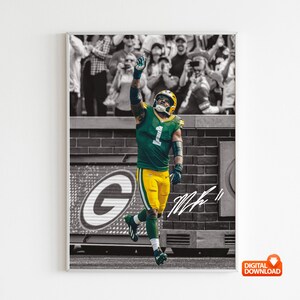 May include: A framed digital download print featuring a football player in a green and yellow uniform, raising his arm in celebration. The background is a black and white image of a crowd. The player's signature is visible.
