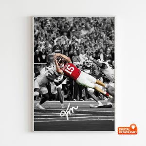 Pode incluir: Fotografia a preto e branco emoldurada de um jogo de futebol americano. Um jogador com uma camisola vermelha com o número 15 mergulha para a frente para apanhar a bola. A imagem é definida com uma multidão nas bancadas.