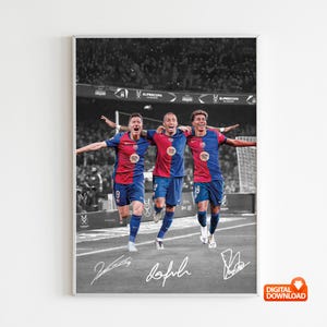 May include: A framed print featuring three soccer players in red and blue jerseys, celebrating a victory. The background is in grayscale, with the players in full color. The print includes signatures and a digital download icon.