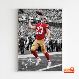 May include: A framed print featuring a football player in a red jersey with the number 23, catching a football. The background is in black and white, with the player in color. The print includes a signature at the bottom.