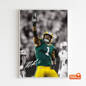 Può includere: Fotografia in bianco e nero incorniciata di un giocatore di football americano in uniforme verde e gialla, che alza il dito indice. Il giocatore indossa un casco e il numero 1 è visibile sulla sua maglia. L'immagine include una firma.