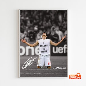 Puede incluir: Una foto en blanco y negro de un jugador de fútbol celebrando un gol. El jugador lleva una camiseta blanca con las palabras "I Belong To Jesus" impresas en ella. El jugador levanta los brazos en el aire y tiene una expresión decidida en su rostro.