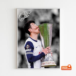 May include: A framed digital download print featuring a soccer player kissing a trophy. The player is wearing a white and navy blue jersey. The background is black and white. A signature is in the upper left corner.