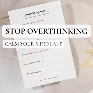 Op de afbeelding: Een wit notitieblok met de tekst "Overthinking Reset" en aanwijzingen om de geest te kalmeren. Het notitieblok heeft de woorden "STOP OVERTHINKING" en "CALM YOUR MIND FAST" in grote, vette letters. Het notitieblok ligt op een neutraal gekleurd oppervlak.