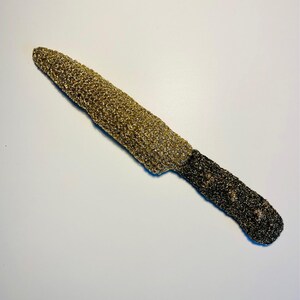 May include: A decorative knife featuring a blade covered in gold glitter and a dark brown glitter-covered handle. The knife is set against a white background.