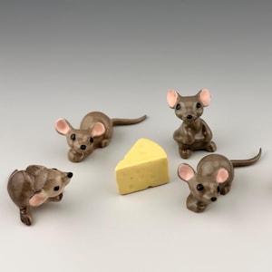 May include: Five small, brown ceramic mouse figurines with pink ears and black eyes arranged around a single triangular piece of yellow cheese. Each mouse is depicted in a different pose, including sitting, lying down, and looking in various directions.