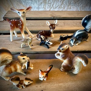May include: A collection of ceramic woodland animal figurines, including a deer, a squirrel, a skunk, and a raccoon. The figurines are painted in realistic colors and have detailed features.