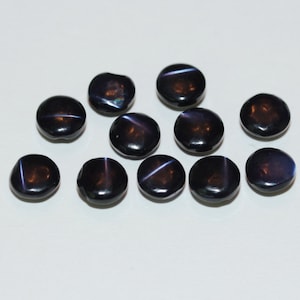 May include: A collection of dark, glossy, round beads with a subtle star-like pattern. The beads have a deep, rich color with hints of blue and purple, and a smooth, polished surface. These beads are likely used for jewelry making.