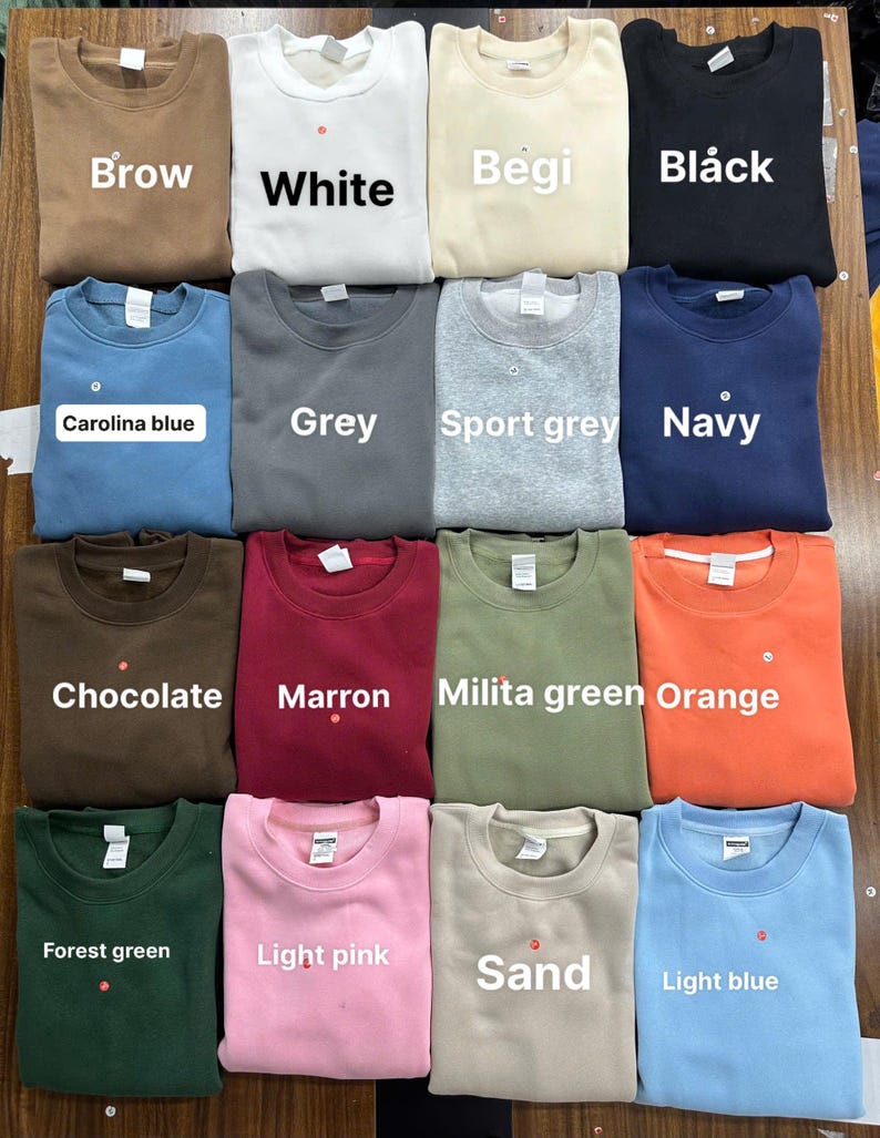 May include: A collection of crewneck sweatshirts in various colors, including brown, white, beige, black, Carolina blue, gray, sport gray, navy, chocolate, maroon, military green, orange, forest green, light pink, sand, and light blue. Each sweatshirt has a tag.