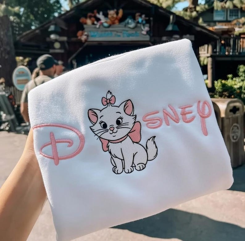 Peut inclure: Sweat-shirt blanc avec une image brod&eacute;e de Marie, le chat des Aristochats de Disney, avec un n&oelig;ud rose et le mot "Disney". Le logo Disney est &eacute;galement brod&eacute; en rose.