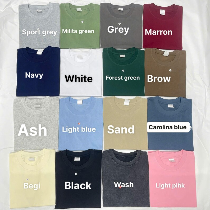 May include: A collection of various colored t-shirts, including sport grey, navy, white, ash, light blue, sand, begi, black, wash, and light pink. Each shirt is neatly folded and labeled with its color name. The shirts are displayed on a white surface.