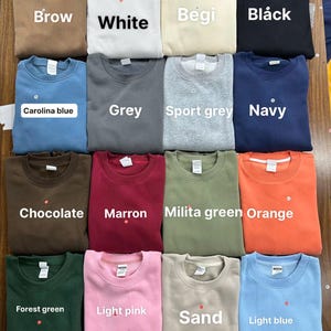 May include: A collection of crewneck sweatshirts in various colors, including brown, white, beige, black, Carolina blue, gray, sport gray, navy, chocolate, maroon, military green, orange, forest green, light pink, sand, and light blue. Each sweatshirt has a tag.