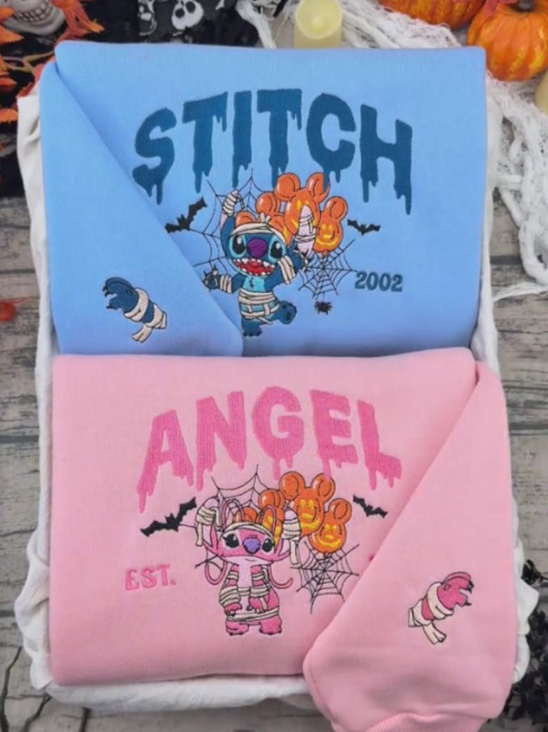 May include: A light blue sweatshirt featuring a blue Stitch graphic wrapped in bandages with orange balloons and the text STITCH 2002, and a pink sweatshirt featuring a pink Angel graphic wrapped in bandages with orange balloons and the text ANGEL EST.