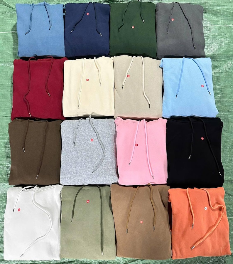 Peut inclure: Une collection de sweats &agrave; capuche pli&eacute;s de diff&eacute;rentes couleurs, dont le bleu, le vert, le rouge et le rose. Chaque sweat &agrave; capuche a une capuche &agrave; cordon de serrage et un petit d&eacute;tail circulaire rouge pr&egrave;s de la poitrine. Les sweats sont dispos&eacute;s avec soin.