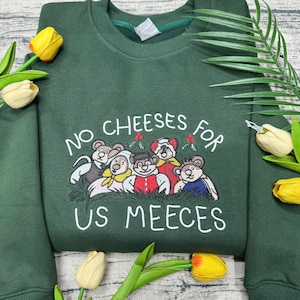 May include: Dark green sweatshirt featuring the embroidered text "NO CHEESES FOR US MEEECES" and a cartoon bear graphic. The sweatshirt has a crew neck and long sleeves. The design is in white.