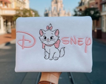 May include: White rectangular item with a pink embroidered Disney logo and the word "SNEY". The item features an embroidered image of Marie, the white kitten from Disney's Aristocats, with a pink bow.