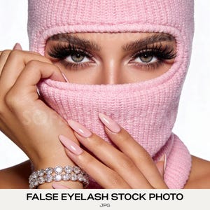 Könnte beinhalten: Nahaufnahme einer Person mit einer rosa Strick-Balaclava, langen, dunklen Wimpern und hellgrünen Augen. Die Person trägt eine rosa Maniküre und ein silbernes Armband mit klaren Steinen. Der Text "FALSE EYELASH STOCK PHOTO" befindet sich unten.