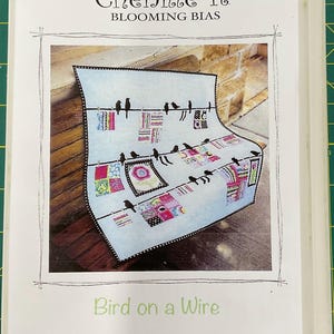 May include: A book cover with the text "Chenille-It BLOOMING BIAS" and a picture of a quilt with birds on a wire. The quilt has colorful squares and a floral design. The title "Bird on a Wire" and the number "#C-730" are also visible.