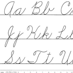 May include: A white fabric featuring black cursive alphabet letters arranged in three horizontal rows. The letters include uppercase and lowercase pairs from A to U. A ruler measuring in inches is visible along the bottom edge of the fabric.