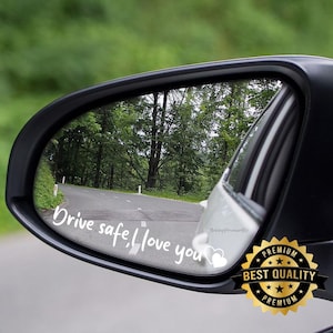 May include: A car side mirror with the text "Drive safe, I love you" in white script. The mirror reflects a road winding through a forest. A "Best Quality" sticker is in the lower right corner.