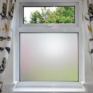 Puede incluir: Una ventana con marco blanco y vidrio esmerilado. La ventana da a árboles verdes. Cortinas con un estampado de hojas enmarcan la ventana.