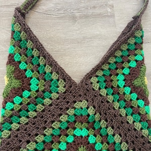 Puede incluir: Un bolso de hombro de crochet marrón, verde y amarillo con un patrón geométrico.