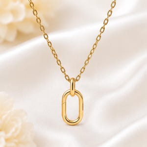 May include: A gold-toned necklace featuring a delicate cable chain and a single, smooth, vertically oriented oval link pendant. The metal has a polished, reflective finish, and the pendant is securely attached to the chain by a small, integrated loop.