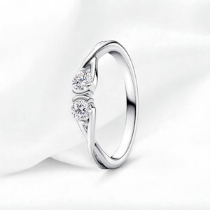 Op de afbeelding: Een zilveren ring met twee ronde, heldere edelstenen. De band van de ring heeft een gedraaid ontwerp en de edelstenen zijn zo gezet dat ze lijken te zweven. De ring wordt gepresenteerd op een witte, getextureerde ondergrond.