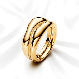 May include: A gold ring with a smooth, flowing design. The ring features two intertwined bands, creating a wave-like appearance. The polished surface reflects light, highlighting the ring's curves and overall shape. The ring is a piece of jewellery.