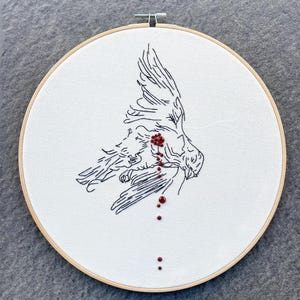 Könnte beinhalten: Stickerei eines Vogels im Flug mit roten Perlen, die Blut darstellen, das von seinem Flügel tropft.