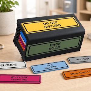 May include: A black desk sign holder with interchangeable rectangular plates. The holder displays "DO NOT DISTURB" in yellow and "BACK SOON" in green. Additional plates include "WELCOME", "IN A MEETING", "You Got This", "Work HARD Dream BIG", and "How Can I Help".
