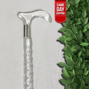 Puede incluir: Bastón de paseo de acrílico transparente con un mango curvo y un eje texturizado. El bastón tiene un collar de metal plateado. La imagen incluye una pancarta roja que dice "SAME DAY SHIPPING".