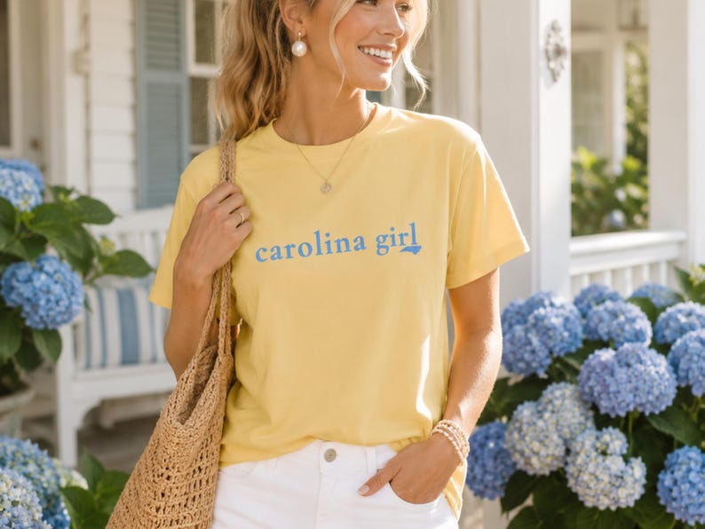 Pu&ograve; includere: Una t-shirt a maniche corte di colore giallo chiaro con la scritta "carolina girl" in lettere blu sul petto. La maglietta presenta un girocollo ed &egrave; abbinata a pantaloni bianchi e a una borsa tote intrecciata color marrone chiaro.