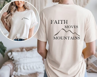 Puede incluir: Camiseta color crema con el texto "FAITH MOVES MOUNTAINS" y un gráfico de montaña. La parte delantera de la camiseta tiene un pequeño gráfico de montaña. Es una prenda informal para el día a día.