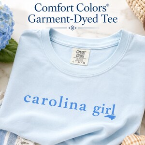 Pu&ograve; includere: Una t-shirt a maniche corte color azzurro con scollo rotondo e finitura tinta in capo. Sul petto presenta la scritta 'carolina girl' in blu pi&ugrave; scuro, con la lettera 'i' sostituita da una piccola sagoma dello stato della Carolina del Nord.