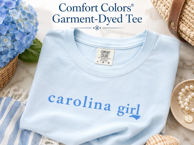 Pu&ograve; includere: Una t-shirt a maniche corte color azzurro con scollo rotondo e finitura tinta in capo. Sul petto presenta la scritta 'carolina girl' in blu pi&ugrave; scuro, con la lettera 'i' sostituita da una piccola sagoma dello stato della Carolina del Nord.