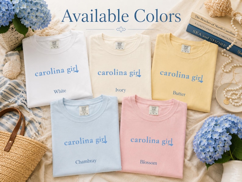 Pu&ograve; includere: Cinque magliette a maniche corte nei colori bianco, avorio, burro, chambray e fiore. Ogni maglietta presenta la scritta 'carolina girl' stampata in blu sul petto. Le magliette sono disposte in gruppo per mostrare le opzioni di colore.