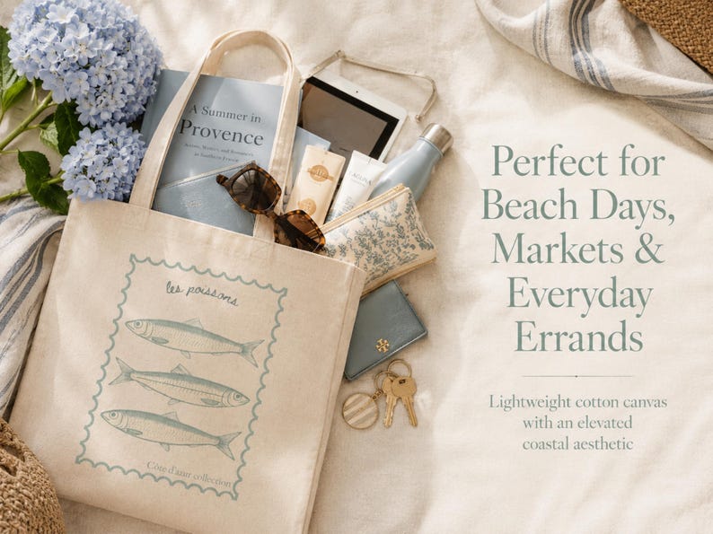 May include: Beige canvas tote bag with a blue fish design, filled with items like sunglasses, a book, and a water bottle. The bag has the text "les poissons" and "A Summer in Provence". Perfect for beach days and errands.