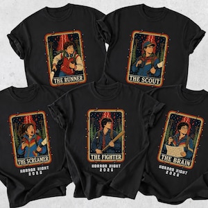 May include: Five black t-shirts featuring graphic prints of characters in retro-style frames. Each shirt displays a unique title: The Runner, The Scout, The Screamer, The Fighter, and The Brain, with the text Horror Night 2026 printed below each.