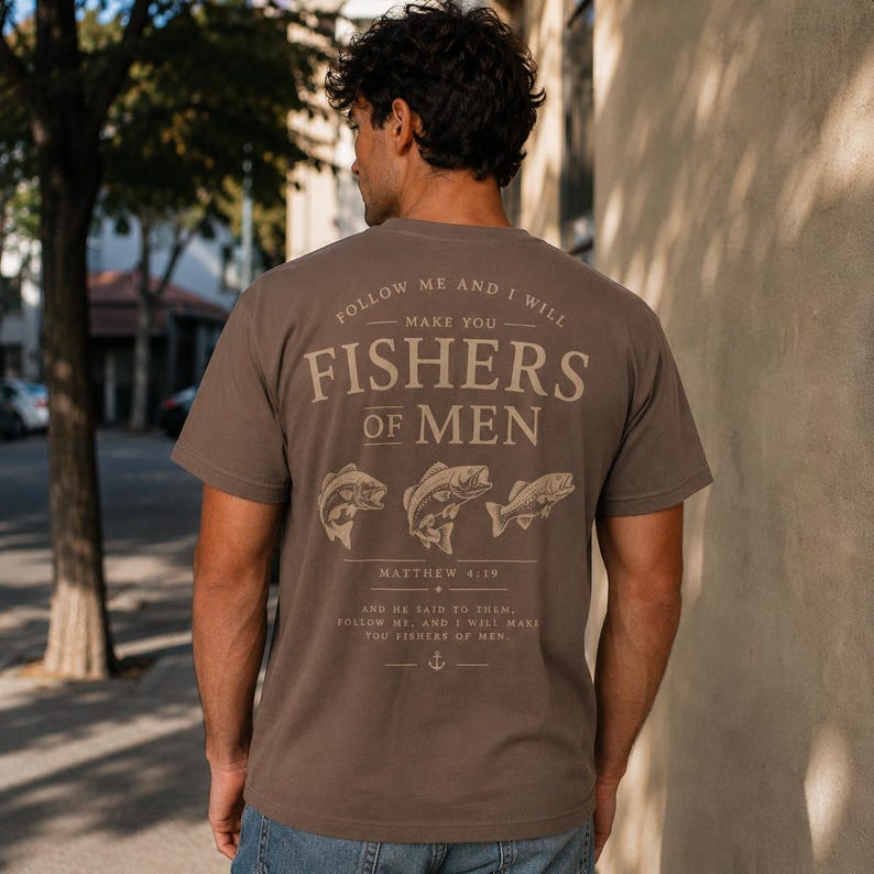 Brown Christian graphic t-shirt mockup displaying Fishers of Men Bible verse artwork with fishing theme, faith-inspired typography and fish illustrations.