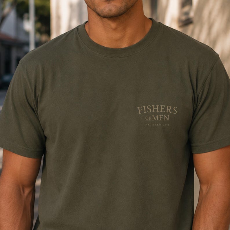 Close-up front mockup of olive green faith-based t-shirt with small Fishers of Men Matthew 4:19 chest graphic, Christian apparel displayed on male model outdoors.