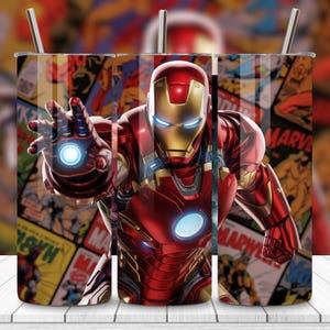 Puede incluir: Un vaso de acero inoxidable con Iron Man en su armadura roja y dorada, con un rayo de energía azul brillante. El fondo es un collage de portadas de cómics vintage. Incluye una pajita plateada.