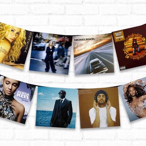 May include: A collection of eight different music album covers hanging on a white brick wall. The albums include Shakira, Avril Lavigne, Nickelback, Kanye West, Alicia Keys, Akon, Craig David, and Beyonce.