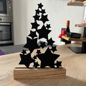 Puede incluir: Objeto decorativo en forma de estrella negra sobre una base de madera. Las estrellas están dispuestas en forma de árbol. La base rectangular de madera tiene vetas naturales.