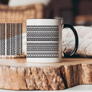 Könnte beinhalten: Weißer Keramikbecher mit schwarzem Henkel und Rand, verziert mit einem schwarz-weißen geometrischen Muster. Der Becher trägt auch den deutschen Text "ICH HASSE MENSCHEN" vertikal gedruckt.