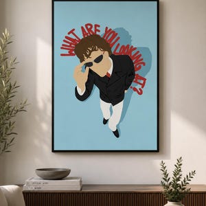 Könnte beinhalten: Ein gerahmter Kunstdruck mit einer stilisierten Illustration einer Person in schwarzem Anzug, weißer Hose und Sonnenbrille vor hellblauem Hintergrund. Der rote Text über der Figur lautet "WHAT ARE YOU LOOKING AT?" in fetter Schrift.