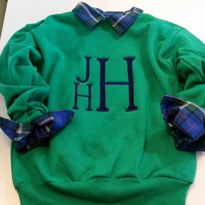 May include: A green sweatshirt with a blue plaid shirt underneath. The sweatshirt has the letters "JHH" embroidered on the front in a large, bold font.